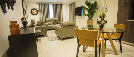 A modern living room with a sofa, armchairs, and a glass dining table.