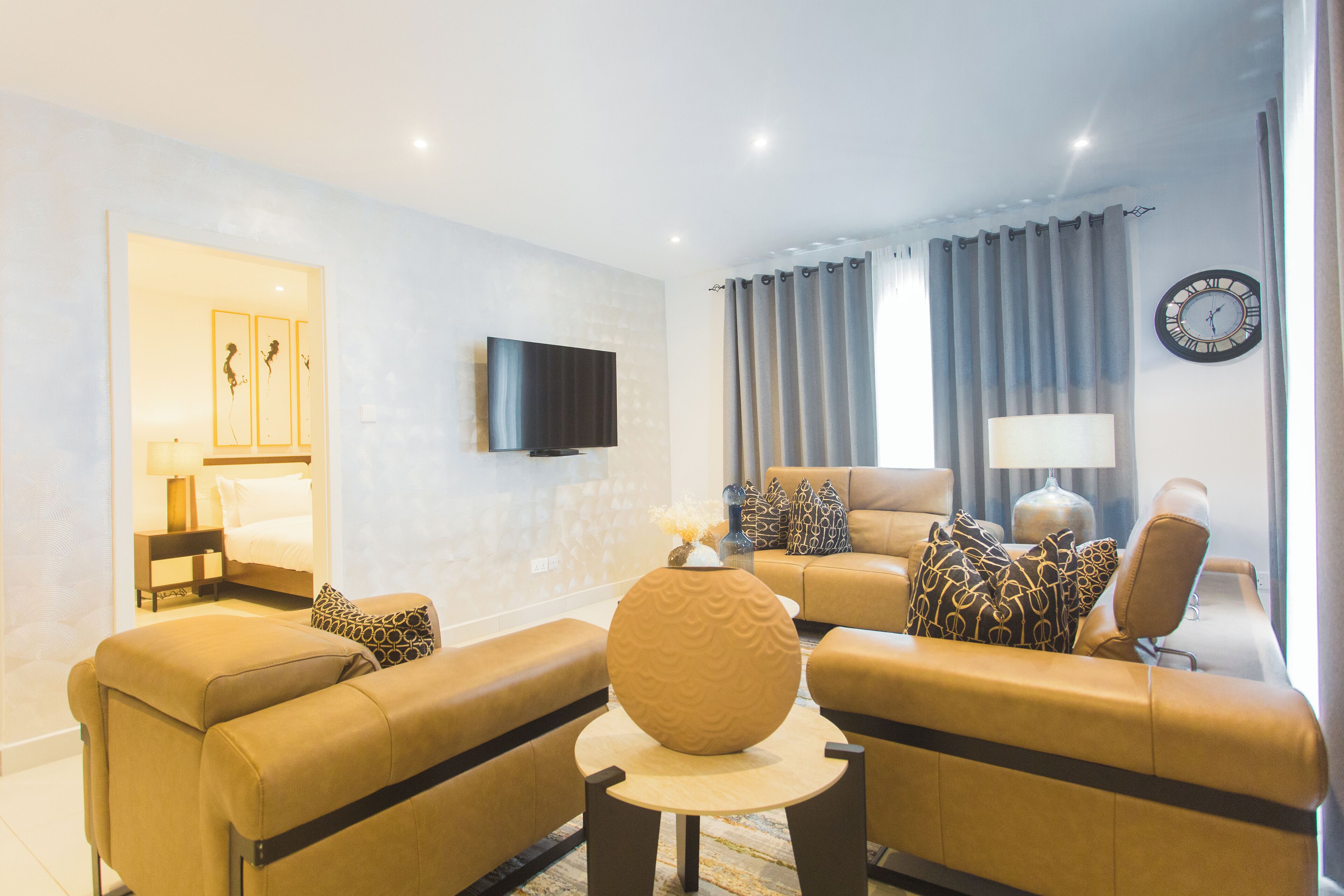 A modern living room with a sofa set, a coffee table, a TV mounted on the wall, and a clock.