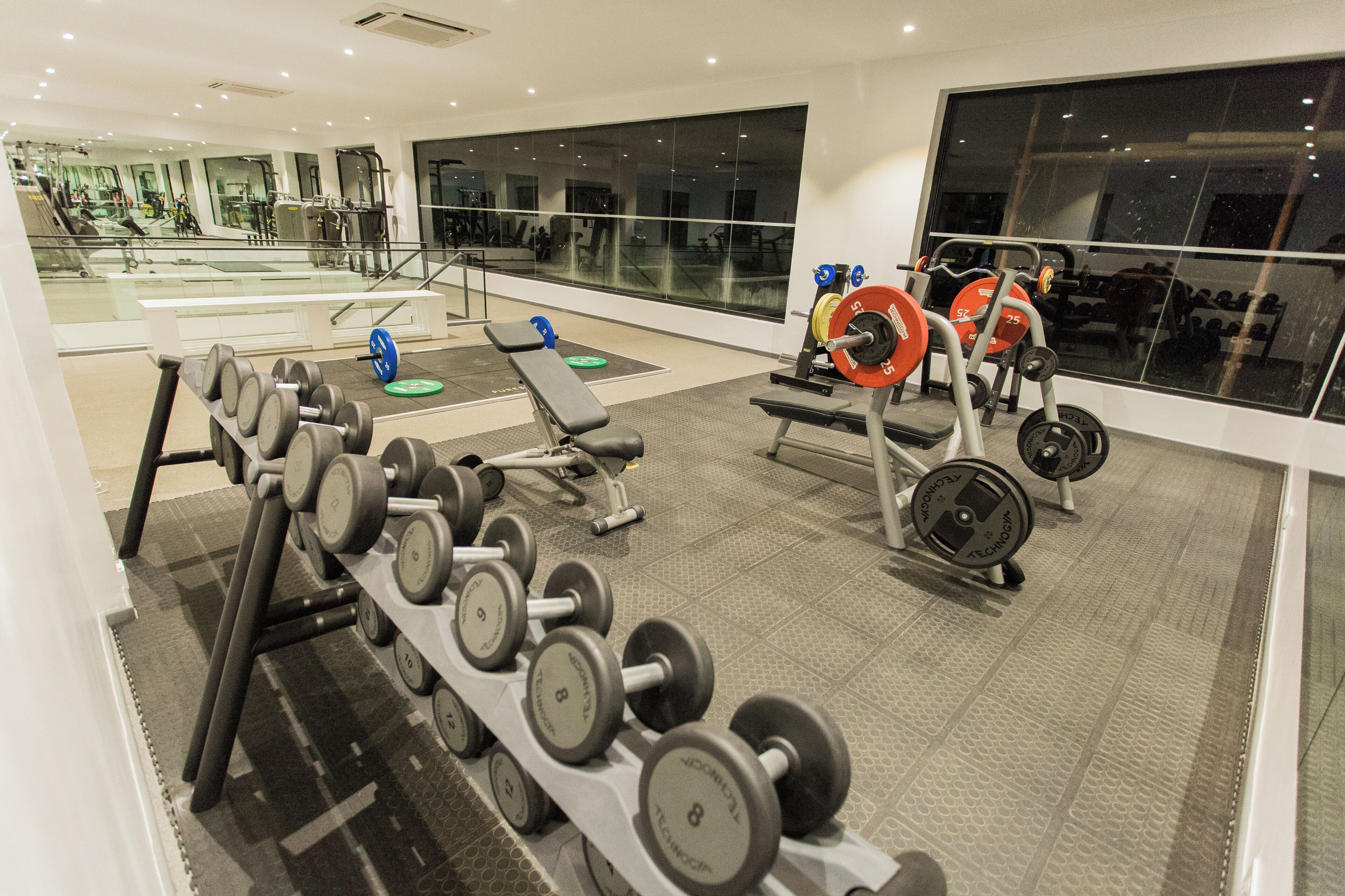 A gym with weightlifting equipment, benches, and a large window.