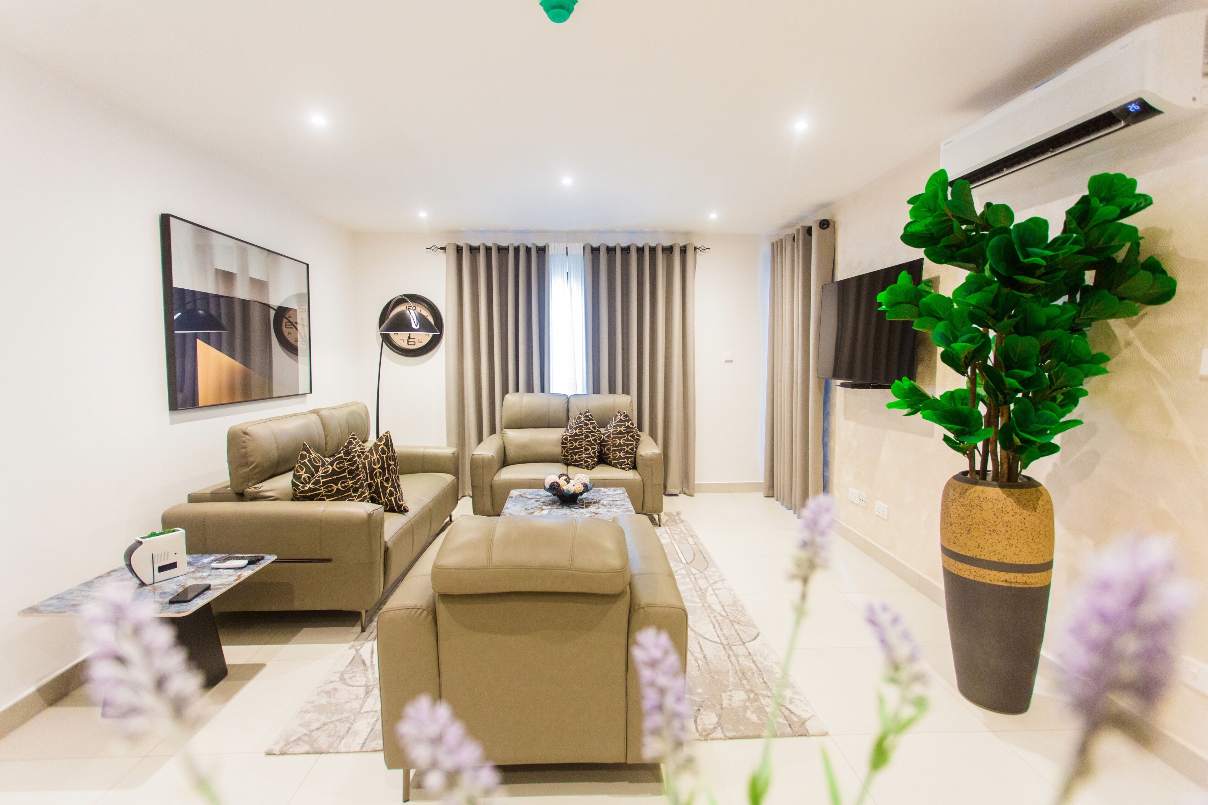 A modern living room with a sofa, armchair, and ottoman, a coffee table, and a potted plant.