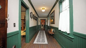 Un couloir avec des lambris verts, un plancher en bois, un tapis à motifs et un banc.