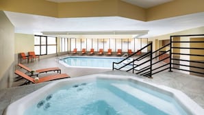 Ein Hotelzimmer mit einem großen Innenpool, Liegestühlen und einer Whirlpool-Badewanne.