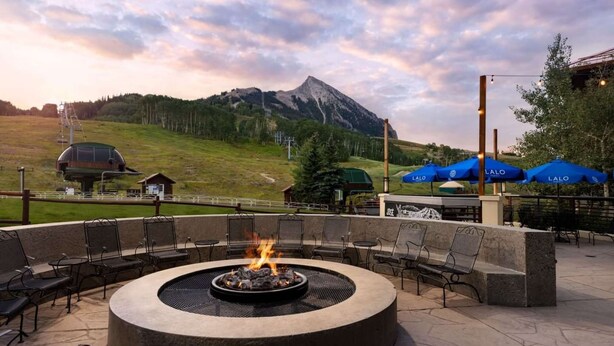 A circular outdoor seating area with a fire pit, surrounded by chairs and tables, overlooking a mountainous landscape. - Near Mt. Crested Butte + Skiing. Dining. Spa. (Mt. Crested Butte)