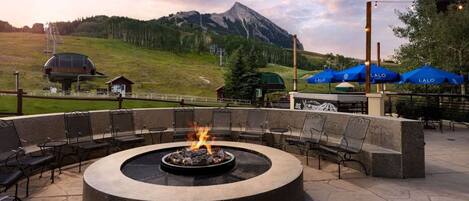 A circular outdoor seating area with a fire pit, surrounded by chairs and tables, overlooking a mountainous landscape.