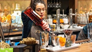 A bar area with a bartender pouring a drink, shelves with various bottles and glasses, and a plate of appetizers on the counter. - Near Mt. Crested Butte + Skiing. Dining. Spa. (Mt. Crested Butte)