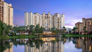 A high-rise hotel with multiple floors, a central courtyard with a reflecting pool, and surrounding greenery. - Close to Disney World + Pools. Spa. Restaurants. (Orlando)