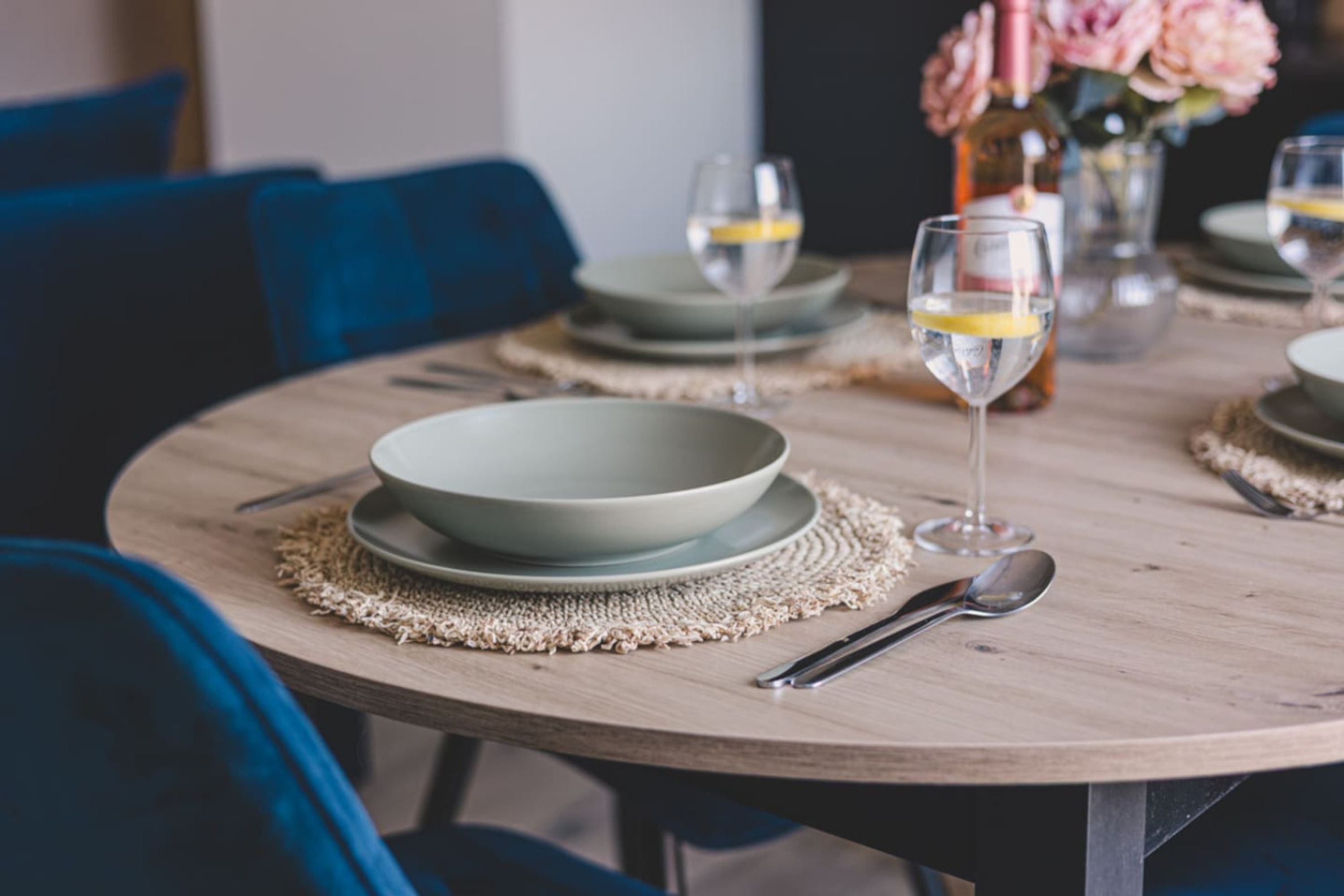 A round dining table with a bowl, a glass, and a spoon on a woven placemat.