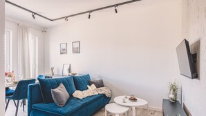 Ein modernes Wohnzimmer mit einem blauen Sofa, einem kleinen runden Tisch und einem an der Wand befestigten Fernseher.