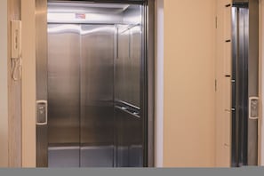 Et elevatorinteriør i metal med et kontrolpanel til venstre og en dør til højre.