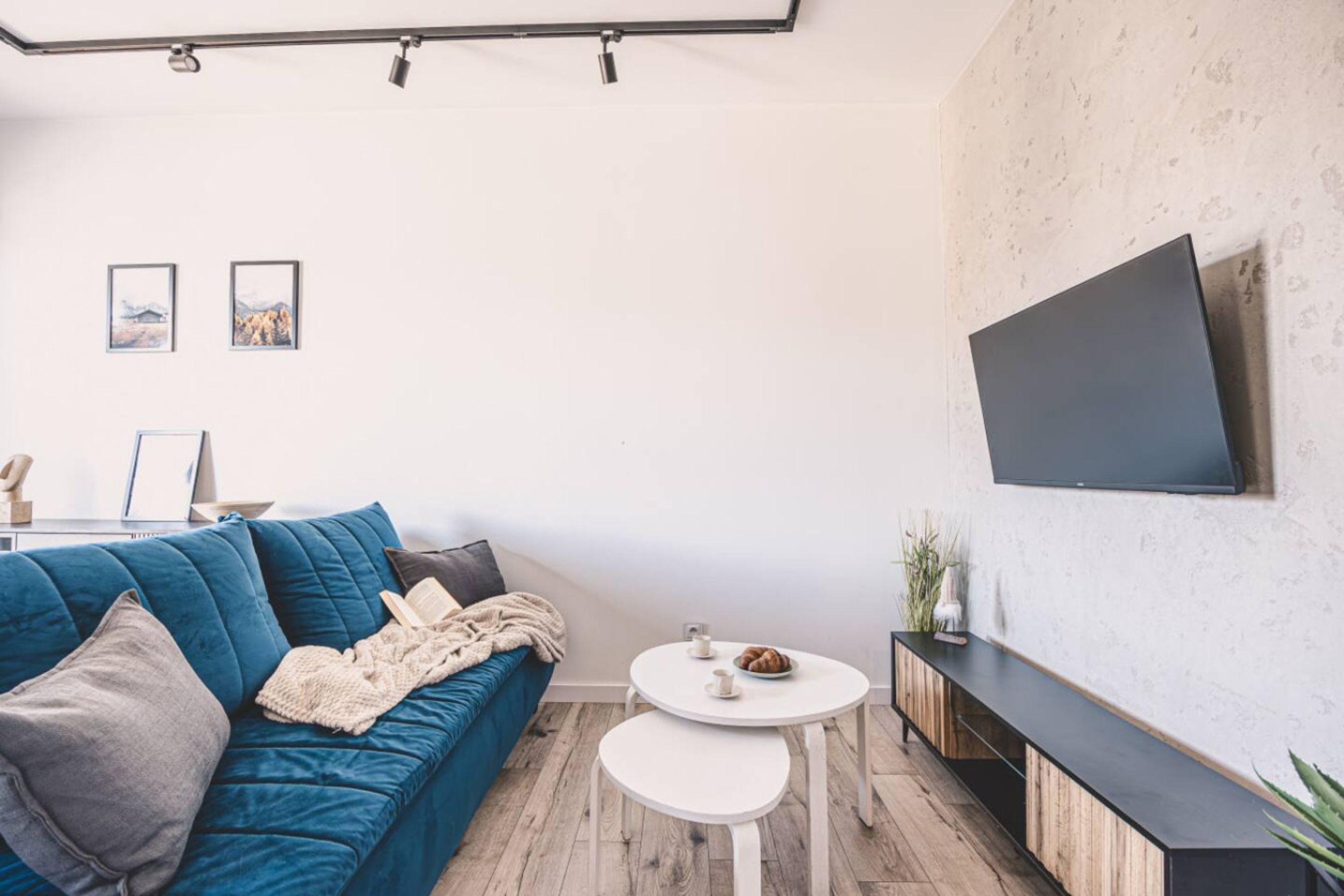 Una sala de estar moderna con un sofá azul, una mesa de centro blanca y un televisor de pantalla plana montado en la pared.