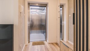Blick ins Innere eines modernen Aufzugs mit Metallverkleidung, Holzboden und einer Tür mit Griff.