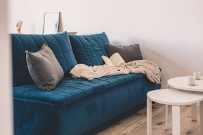 En blå sofa med et beige tæppe og en bog, et lille hvidt bord med kopper, og et trægulv.