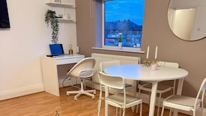 A modern room with a round glass table, white chairs, a white desk, and a large window with a view. - The Cotton Mill Hideaway (Manchester)