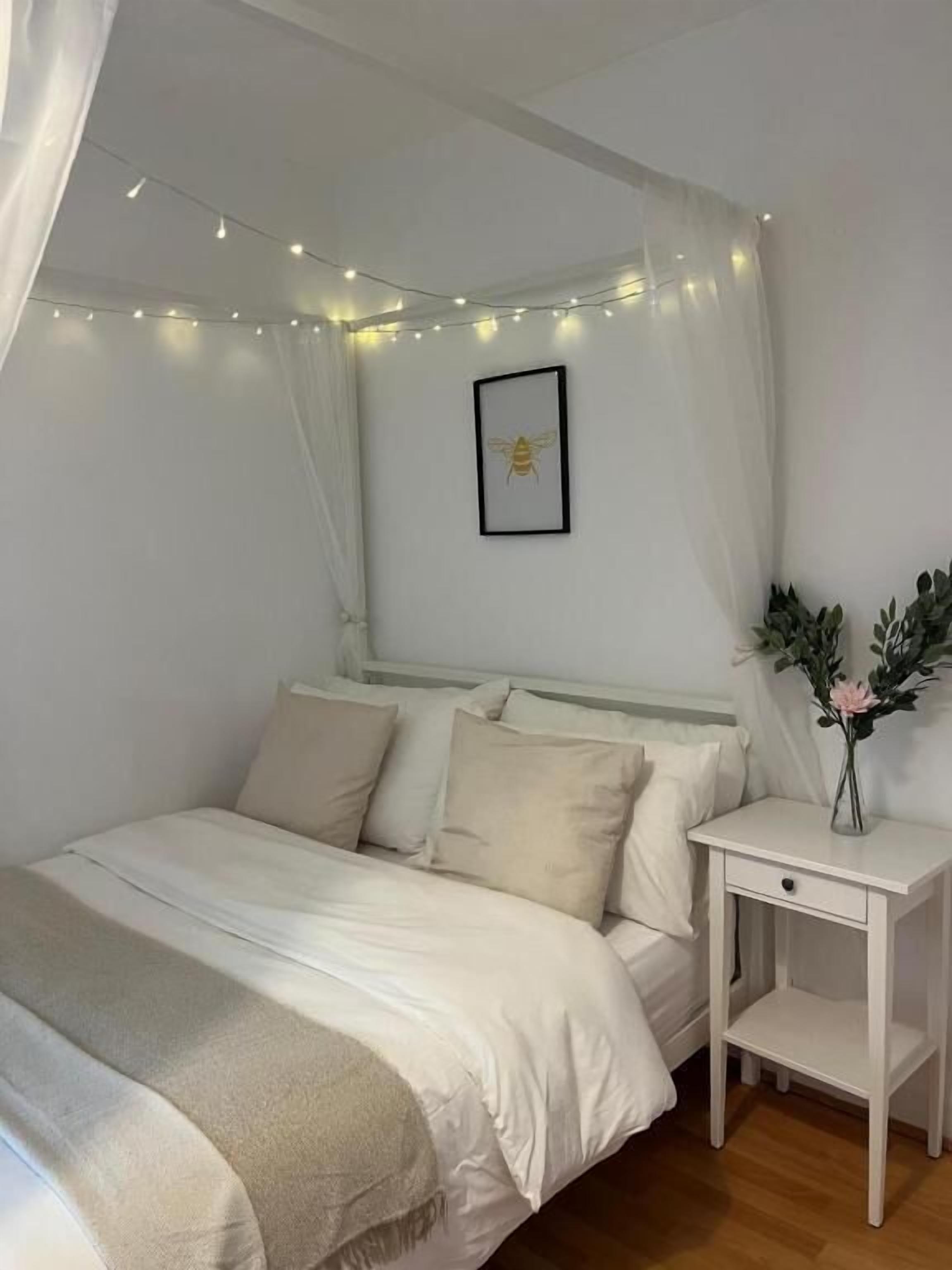 A bedroom with a canopy bed, bedside table, and a framed picture on the wall.