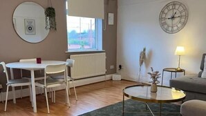 A living room with a round table, a sofa, a clock, and a window with blinds. - The Cotton Mill Hideaway (Manchester)