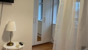 A room with a flat-screen TV mounted on the wall, a small table with a lamp, and a white curtain partially drawn. - The Cotton Mill Hideaway (Manchester)