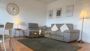 A modern living room with a grey sofa, a coffee table, a clock, and framed pictures on the wall. - The Cotton Mill Hideaway (Manchester)