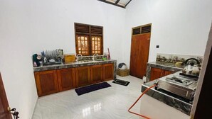 A kitchen with wooden cabinets, a marble countertop, and a window with blinds. - Rivers Edge Resort Sinharaja (Weddagala)