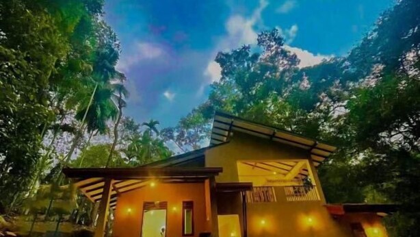 A single-story building with a flat roof, surrounded by lush greenery and palm trees. - Rivers Edge Resort Sinharaja (Weddagala)