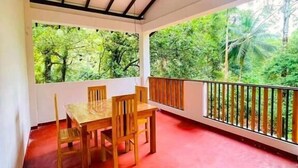 A covered outdoor area with a table and chairs, surrounded by a red floor and a railing overlooking a lush green landscape. - Rivers Edge Resort Sinharaja (Weddagala)