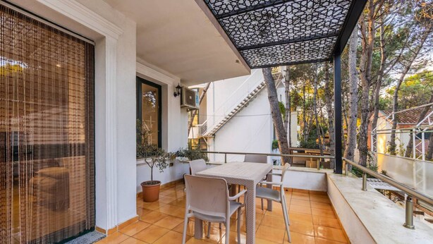 Um pátio com uma mesa e cadeiras, um vaso de planta e uma escadaria que leva a um andar superior.