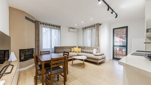 Uma sala de estar moderna com sofá, mesa de jantar e cadeiras. Há uma cozinha com bancada e pia.