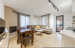 Ein modernes Wohnzimmer mit Sofa, Esstisch und Stühlen. Es gibt eine Küchenzeile mit Arbeitsplatte und Spüle.