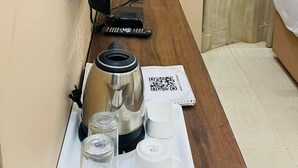 Habitación de hotel con escritorio de madera, cafetera, control remoto y bandeja con vasos y tazas.