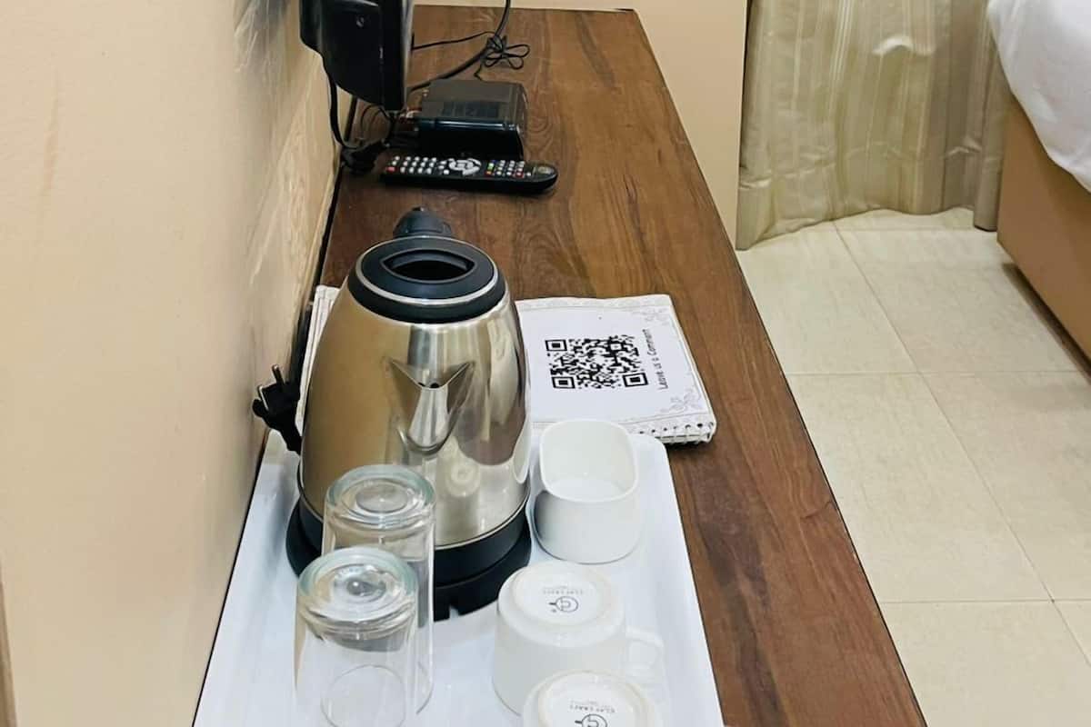 A hotel room with a wooden desk, a coffee maker, a remote control, and a tray with glasses and cups.