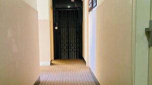 Un pasillo con alfombra estampada, una puerta negra al final y un interruptor de luz en la pared.