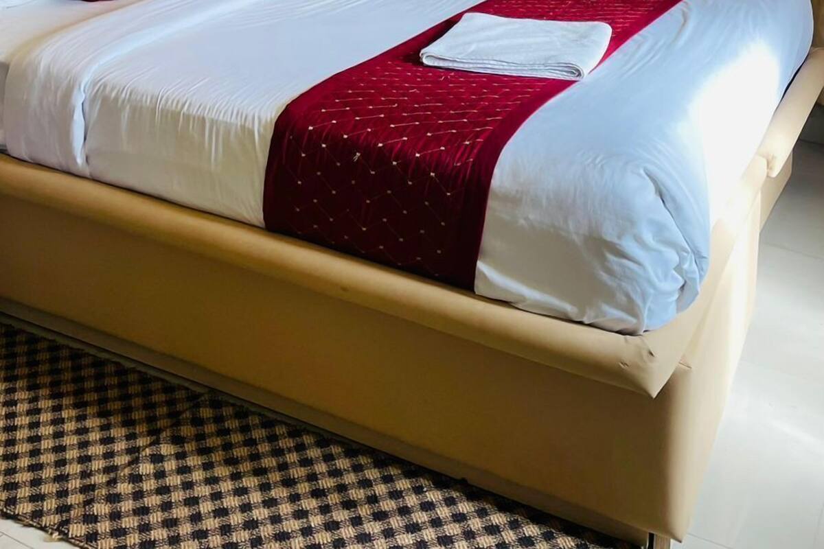A hotel room with a bed, a ceiling fan, an air conditioning unit, and a window with curtains.