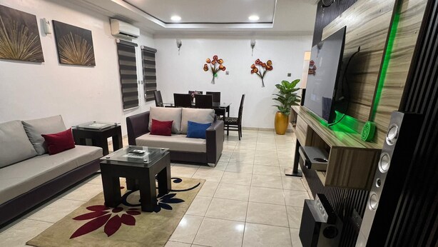 A modern living room with a sofa, coffee table, and a TV stand. - RBZ Apartments (Lagos)
