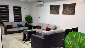 A modern living room with a sectional sofa, a coffee table, and a large plant. - RBZ Apartments (Lagos)