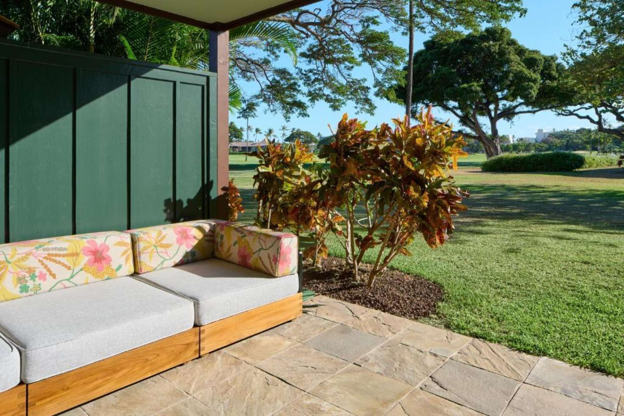 Un espacio de estar al aire libre con techo, un banco de madera y una pared verde de fondo.