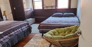 Un dormitorio con dos camas, un armario de madera, una mesita pequeña y una silla de mimbre.