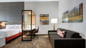 A hotel room with a bed, desk, chair, sofa, and artwork on the walls. - Near Downtown Parker | Free Breakfast + Pool (Parker)