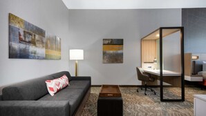 A modern hotel room with a grey sofa, a wooden coffee table, a desk with a chair, and artwork on the walls. - Near Downtown Parker | Free Breakfast + Pool (Parker)
