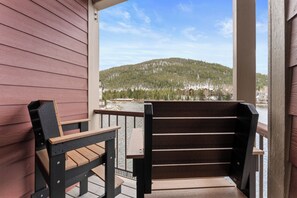 A wooden deck with a bench and a table, overlooking a forested hillside. - Lakefront Condo Near the Slopes - Walk to Shops & Dining (Keystone)