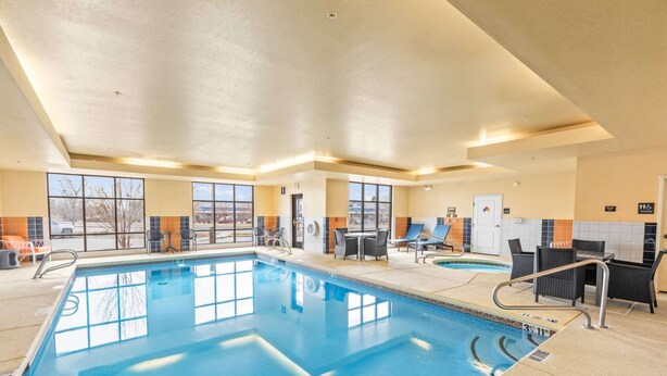 Une piscine intérieure à l’eau claire, entourée de chaises longues et de tables, et dotée de grandes fenêtres qui laissent entrer la lumière naturelle.