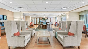 Un hall d’hôtel comprenant deux fauteuils, une table basse, un coin repas et un comptoir d’accueil.