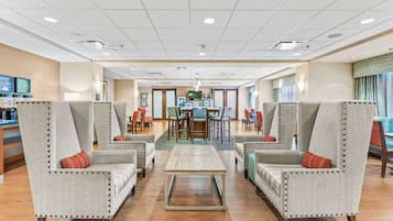 A hotel lobby with two armchairs, a coffee table, a dining area, and a reception desk.