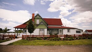 Un edificio de dos pisos con techo rojo, revestimiento blanco y detalles en verde.