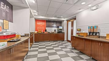 A hotel breakfast area with a checkered floor, a coffee machine, and a waffle station.