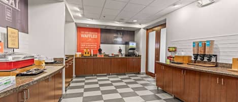 A hotel breakfast area with a checkered floor, a coffee machine, and a waffle station.