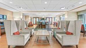 Un vestíbulo de hotel con dos sillones, una mesa de centro, un comedor y una recepción.