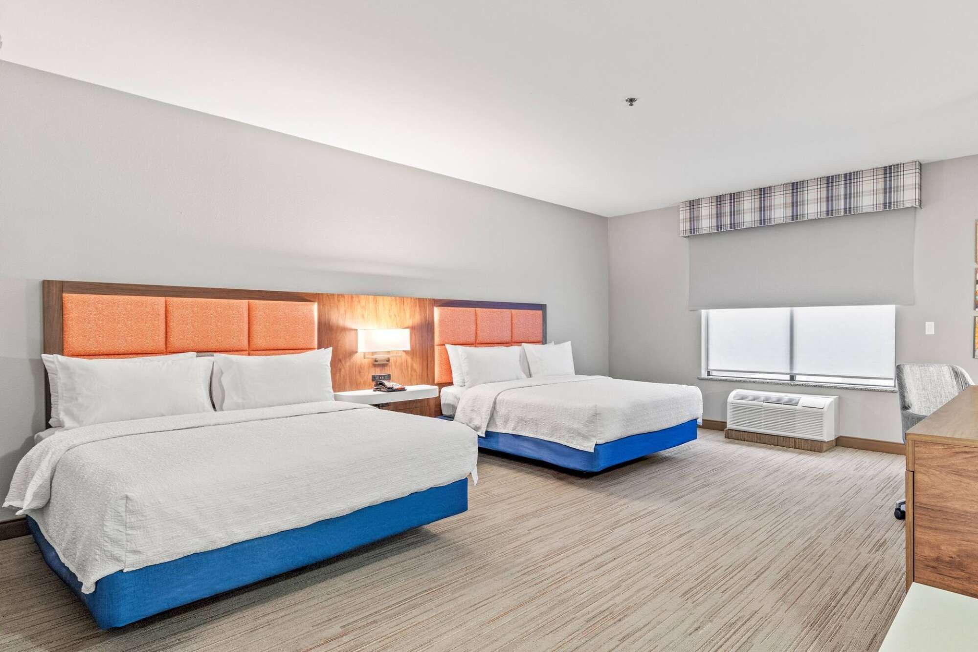 A hotel room with two beds, a desk, and a window with blinds.