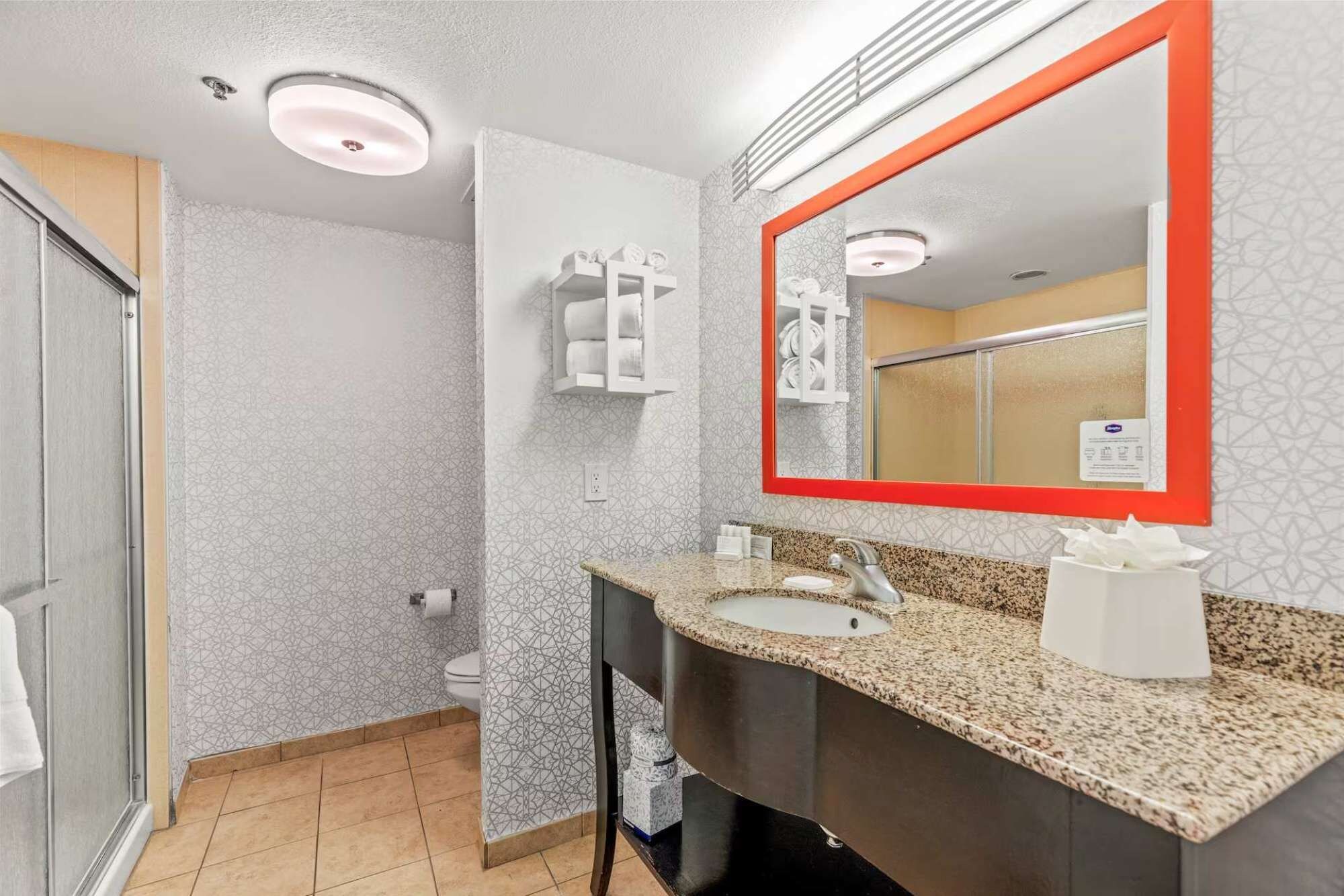 A bathroom with a sink, mirror, towel dispenser, and toilet.