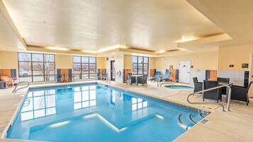 An indoor swimming pool with clear water, surrounded by lounge chairs and tables, and large windows providing natural light.