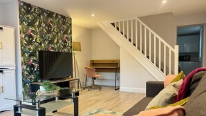 Un salon moderne avec un téléviseur à écran plat, une table basse en verre, un fauteuil rose et un escalier menant à un autre niveau.