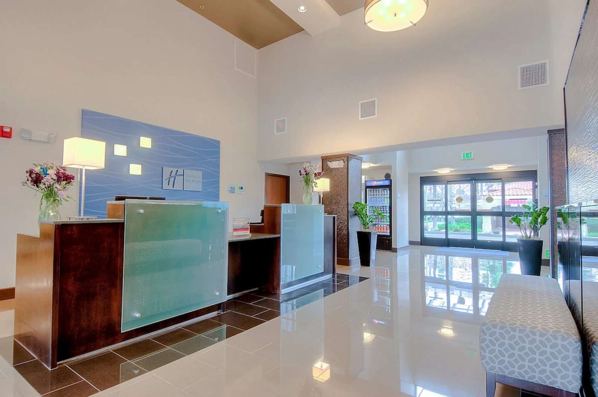A modern reception area with a glass desk, a reception counter, and a seating area with a patterned bench.